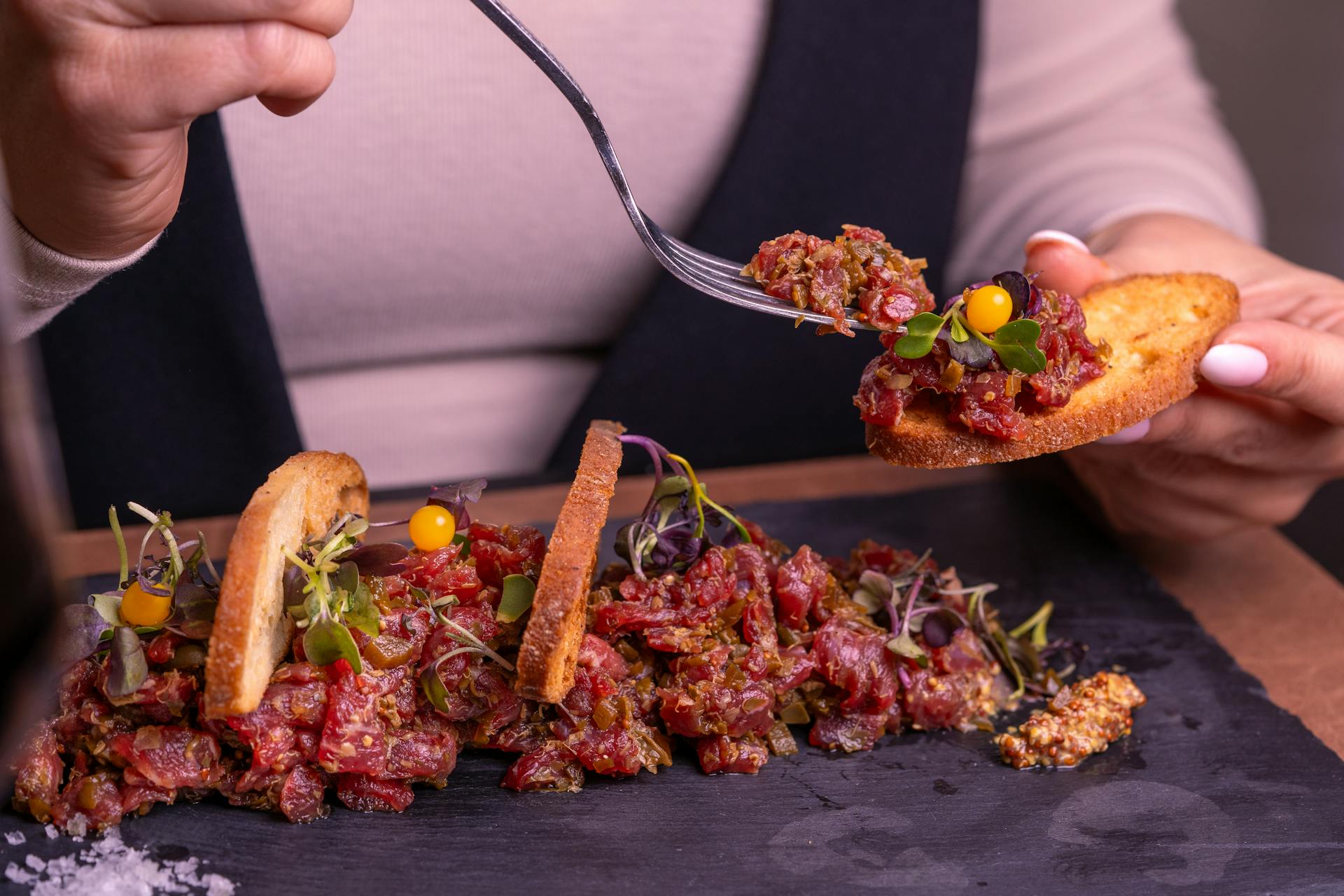 Close-up of gourmet beef tartare served with crostini, herbs, and garnish on a slate plate.