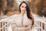 一名年轻女子身着时尚毛衣，在秋叶纷飞的户外摆出姿势，散发着永恒的美丽
