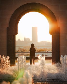 Silhouette of a person at sunset through an archway with fountains in Qatar's vibrant backdrop.