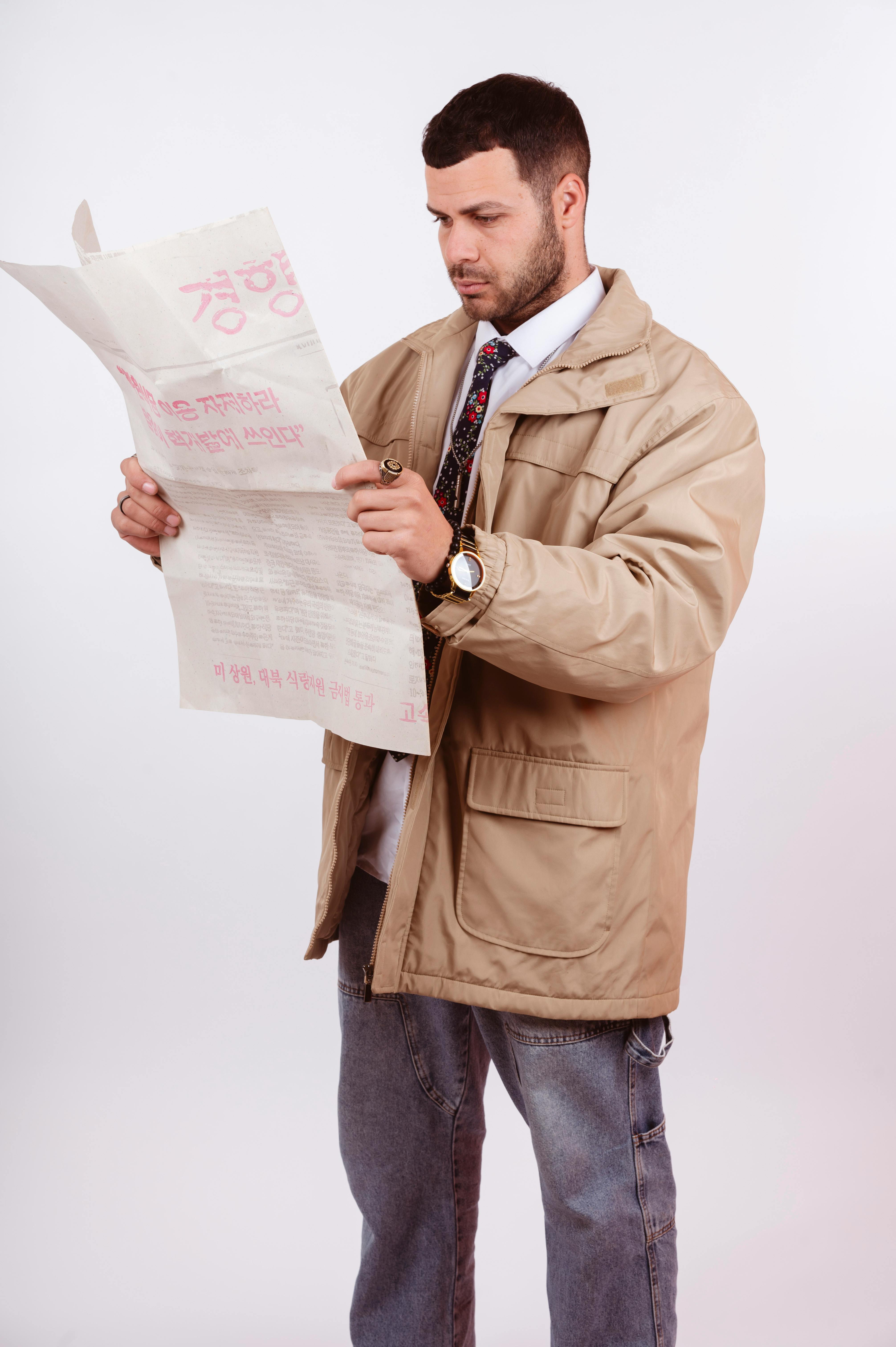 Free Adult male wearing a casual jacket and jeans, reading a newspaper in a studio setting. Stock Photo