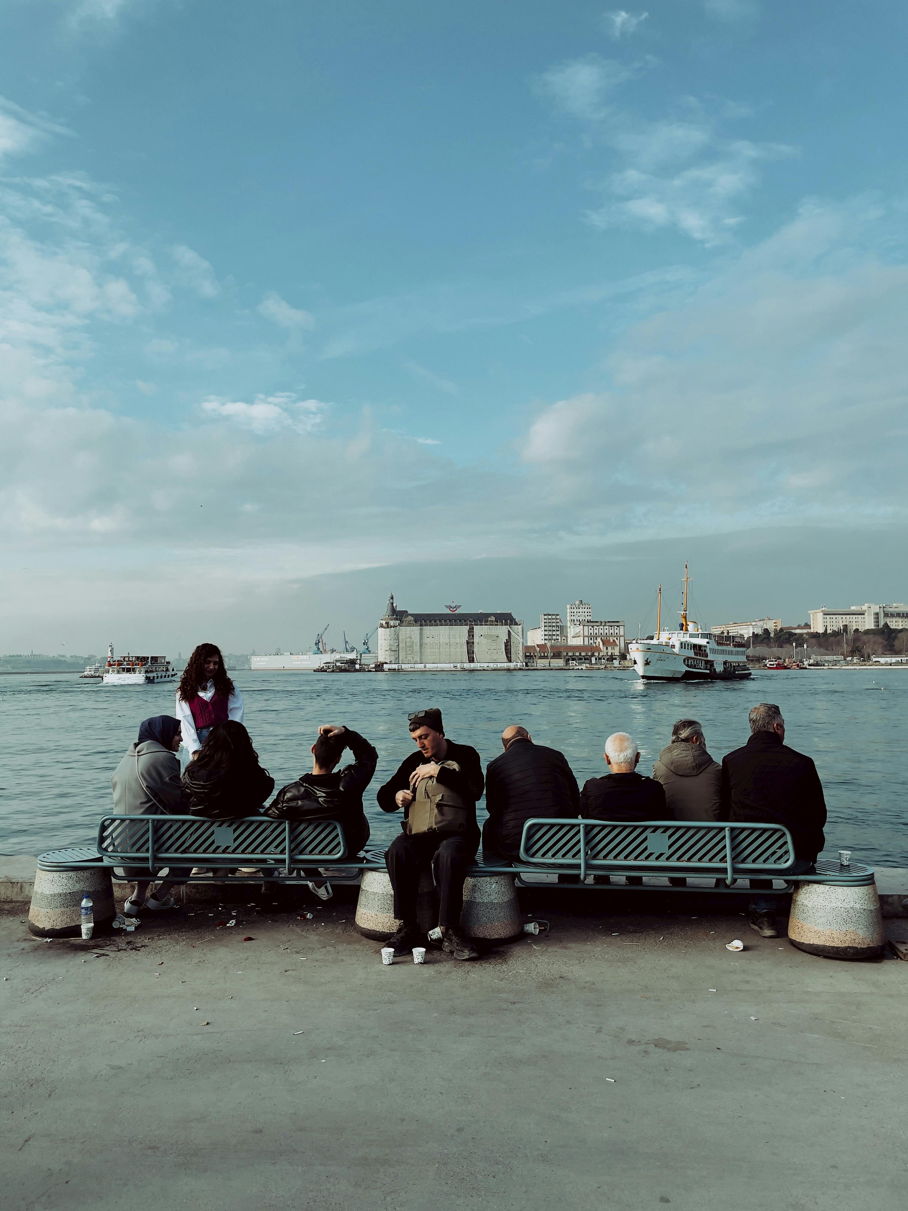 Group of adults seated by the waterfront, enjoying a serene port city view under a clear sky.