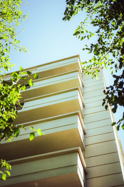 Low-angle view of a modern apartment building in Mendoza, framed by lush green trees.