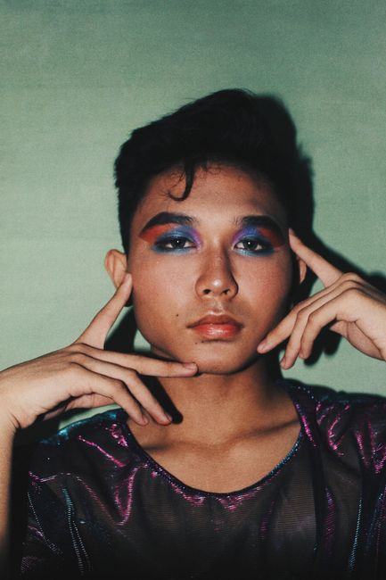 Vibrant portrait of a young Asian model with colorful eye makeup and stylish attire.