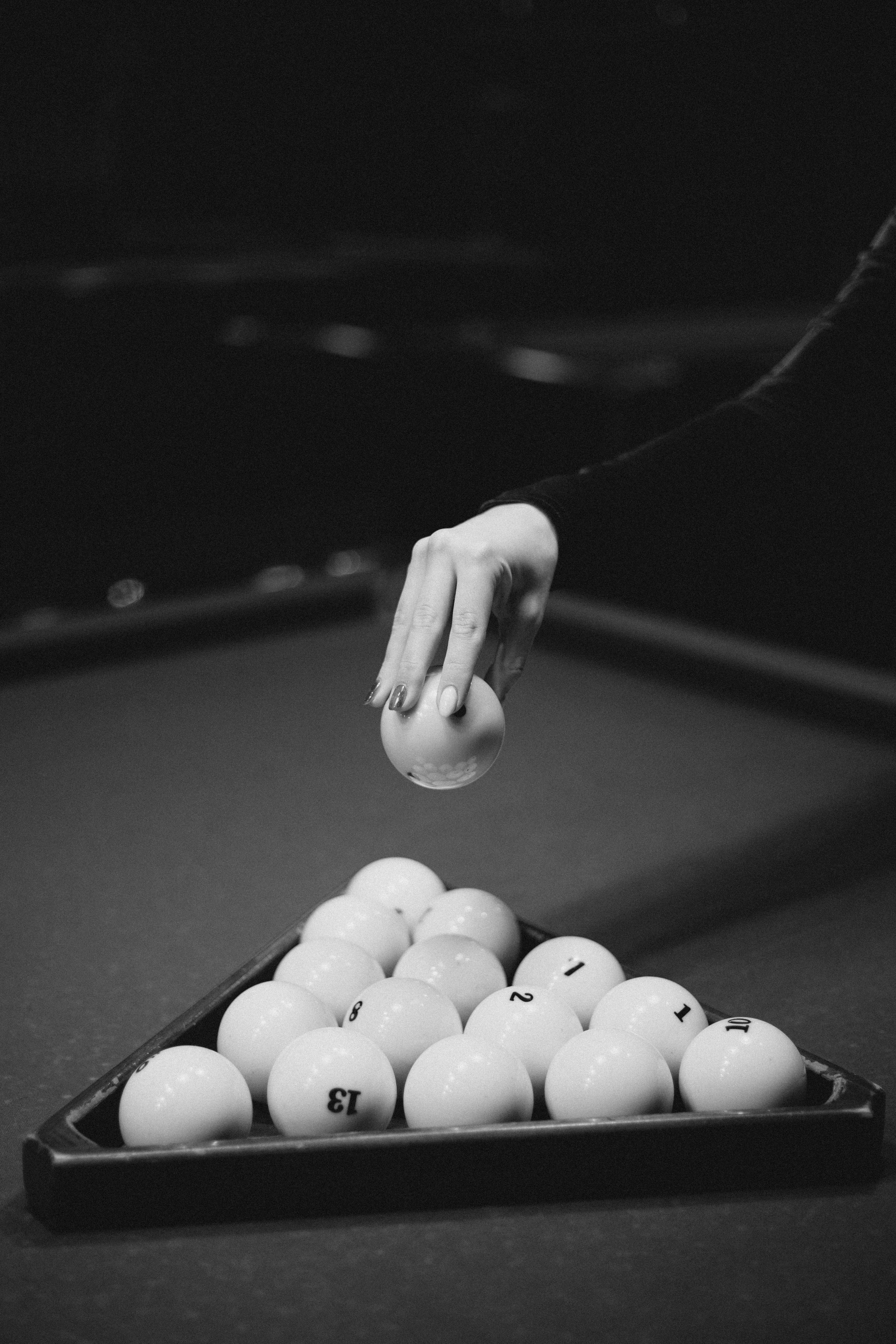 Black and white image of a hand setting billiard balls in a triangle on a pool table.