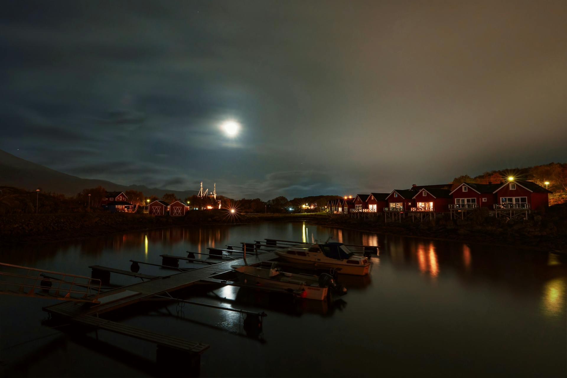 Moonlit view of a tranquil fishing village and pier, with reflections on calm water.