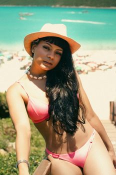 Stylish woman enjoys a sunny day at the beach, wearing a pink bikini and straw hat.
