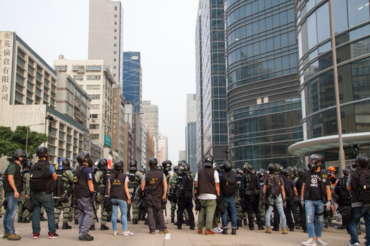 Group of police officers in anti-riot gear standing in the urban area facing a city.
