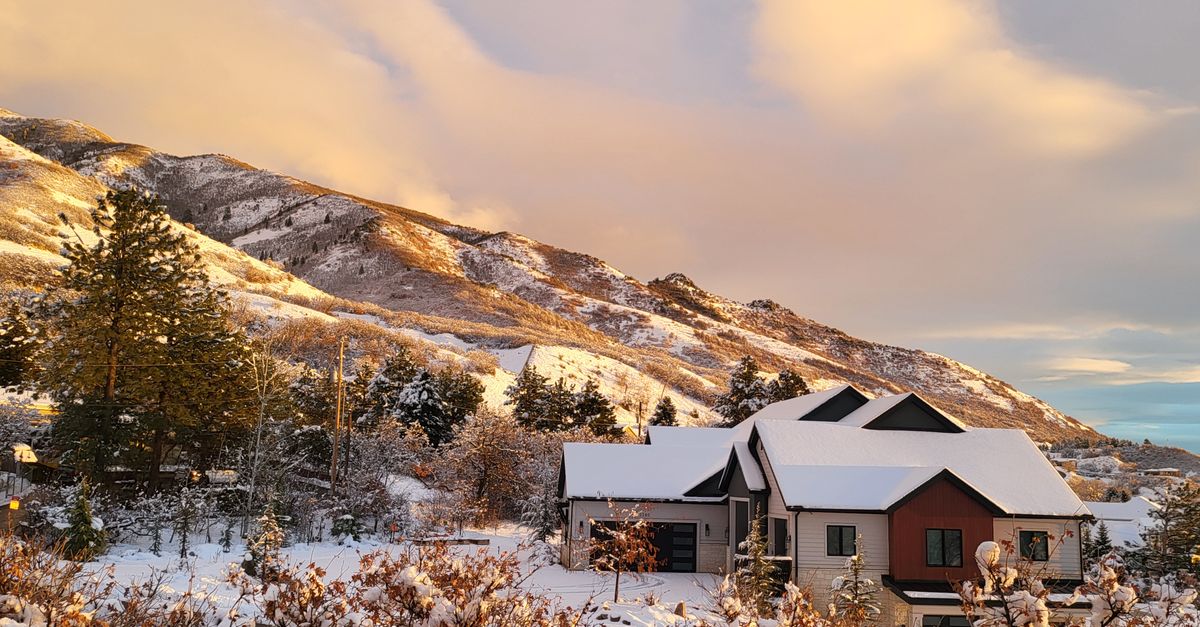 Scenic view of snow-covered mountains and a house under a vibrant sunset sky.