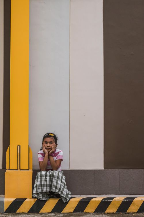 Free A young girl in casual wear sitting on a city curb. Urban setting with thoughtfulness. Stock Photo