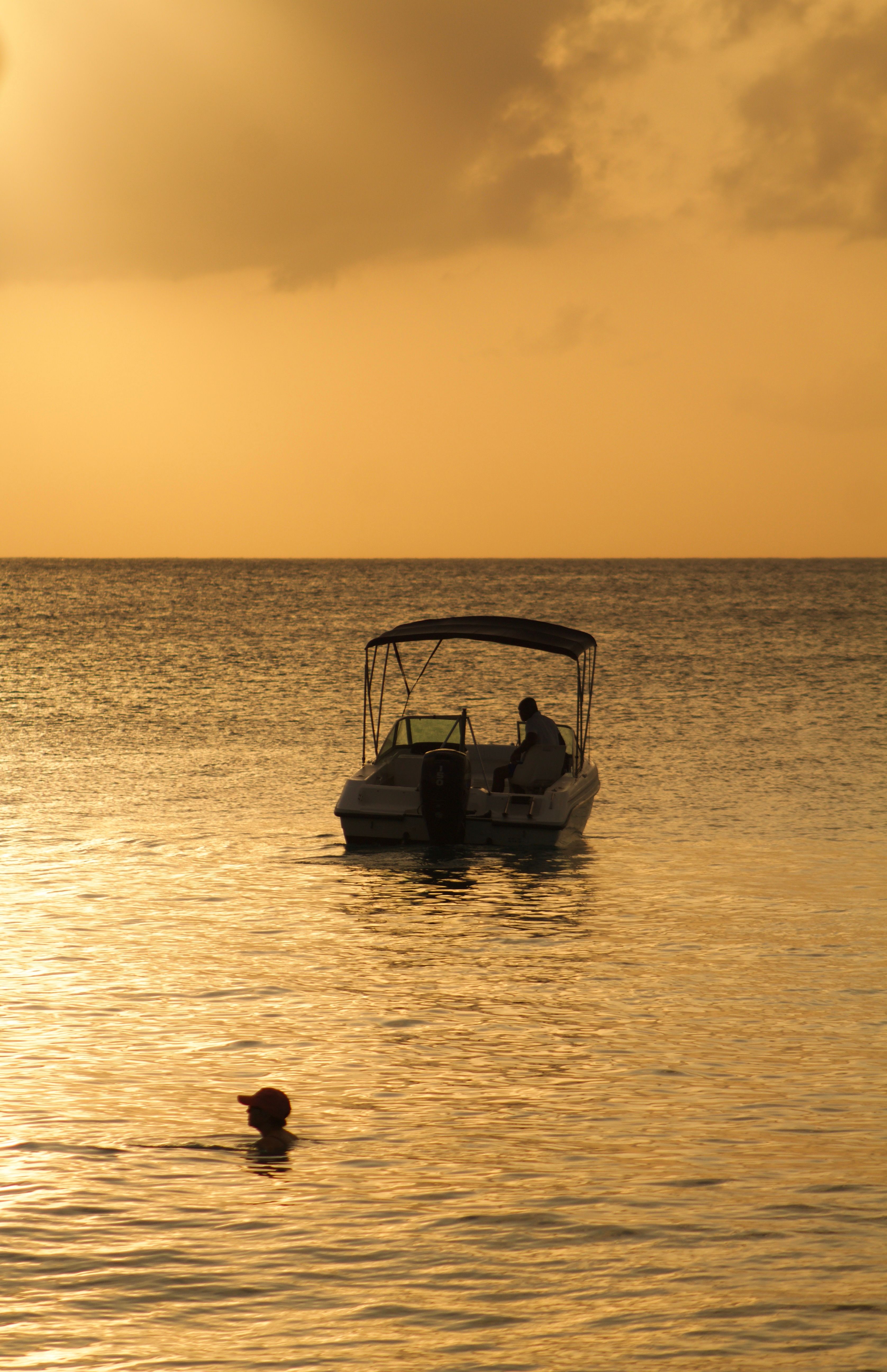 Serene sunset in Barbados featuring a boat and swimmer silhouetted against golden waters. - Is Barbados Safe for Tourists? (Top Ranking)