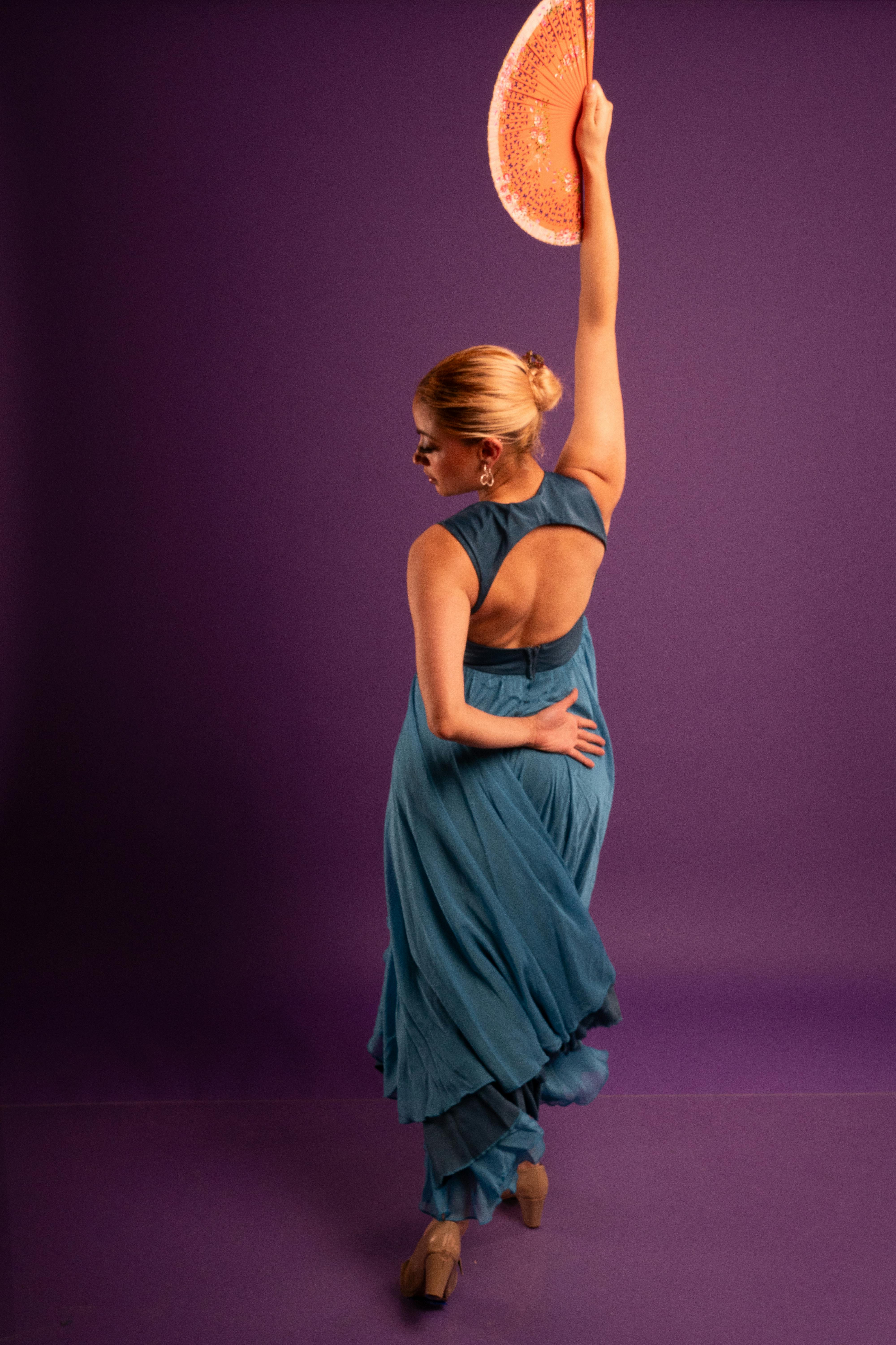 grátis Dançarina de flamenco em vestido azul-petróleo se apresentando com leque em um cenário roxo. Foto profissional