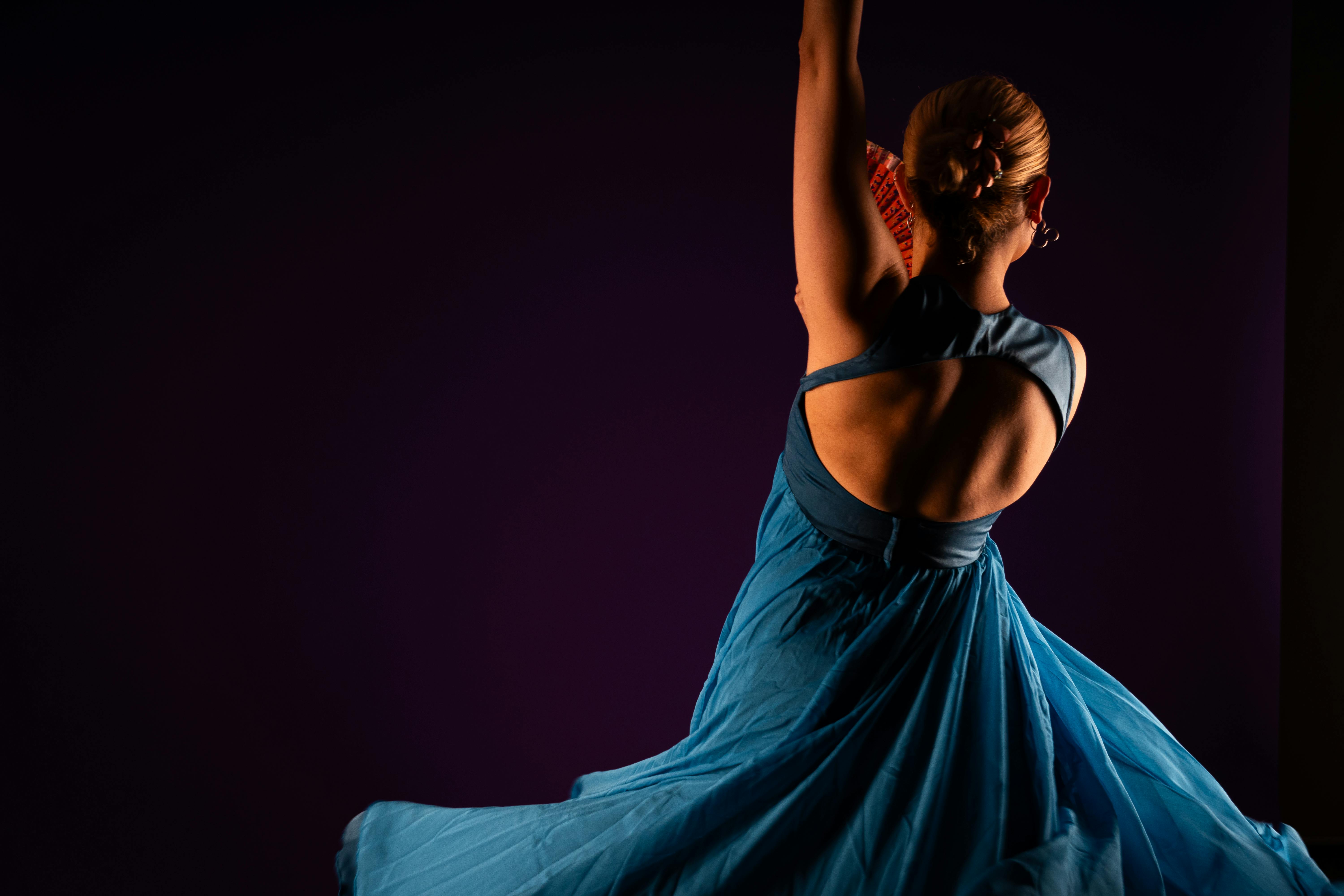 bezplatná Žena elegantně tančí ve splývavých modrých šatech na tmavě fialovém pozadí. Základová fotografie