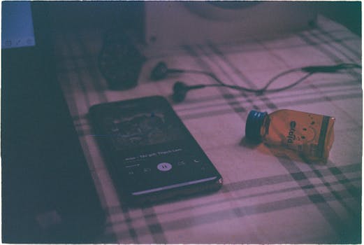 A vintage still life featuring a smartphone, earphones, and a bottle on a plaid surface.