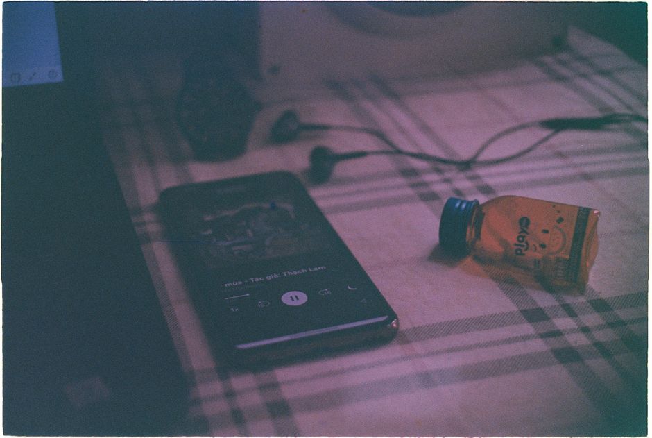 A vintage still life featuring a smartphone, earphones, and a bottle on a plaid surface.