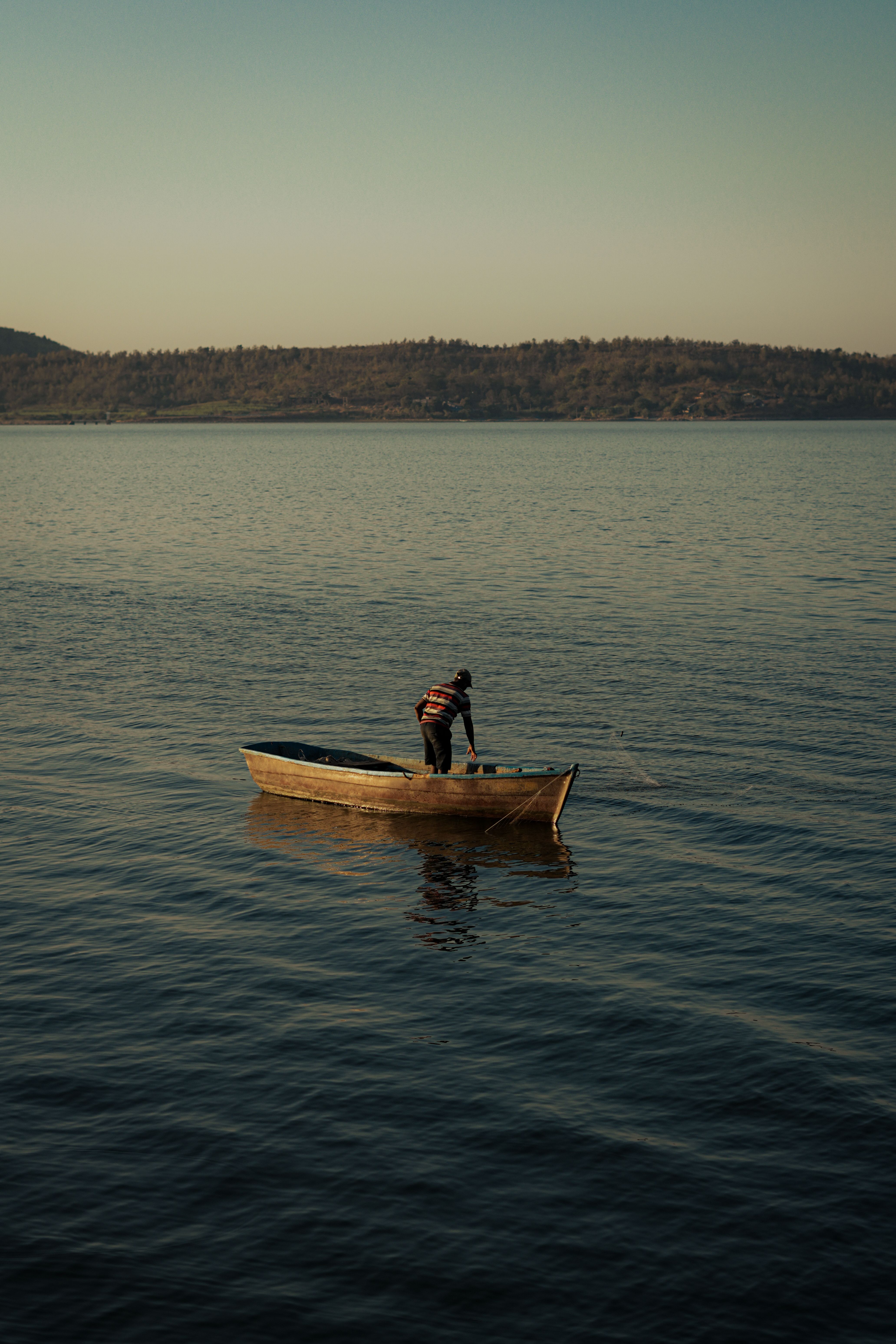A lone fisherman on a wooden boat in Thuti, Gujarat, India, during a serene day. | Indian Village Development