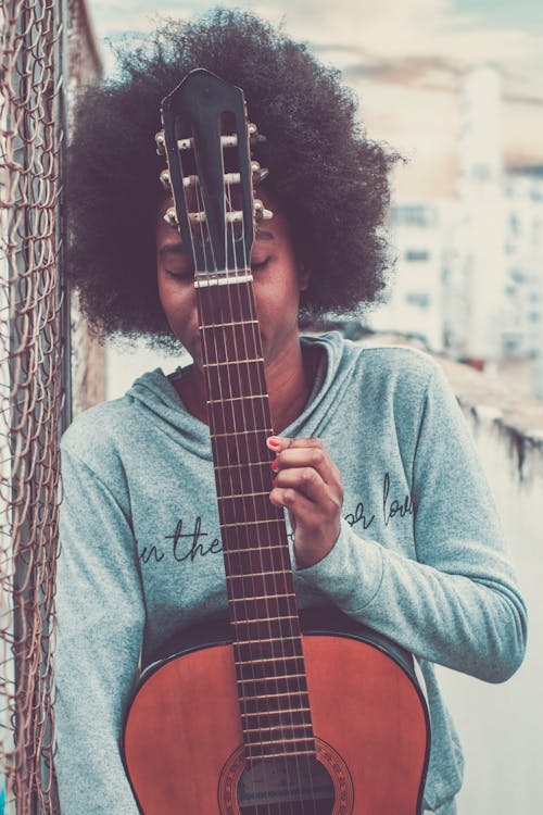 Unrecognizable African American female musician with closed eyes standing on street with acoustic guitar