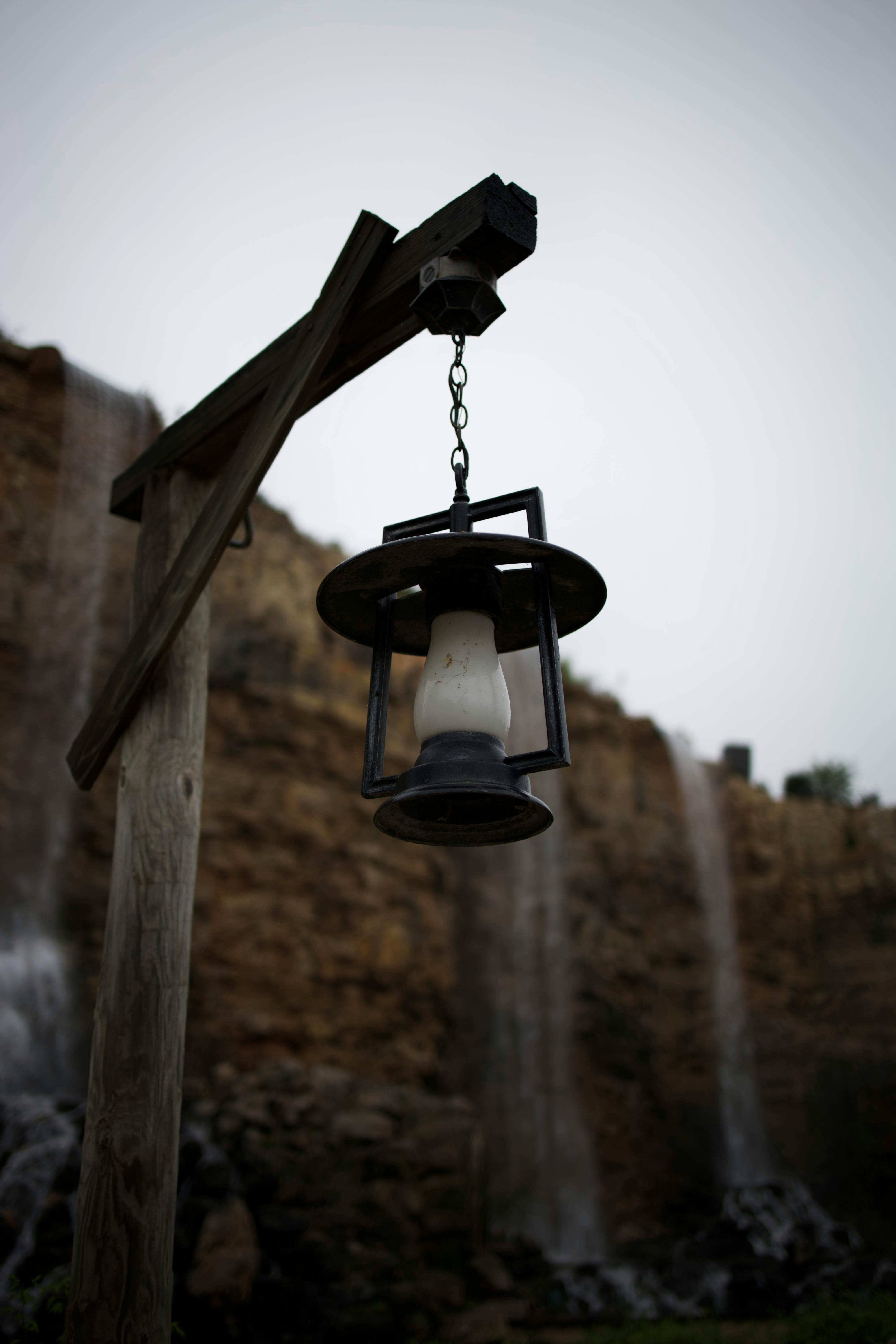 A vintage lantern hangs against a backdrop of a cascading waterfall on a cloudy day.