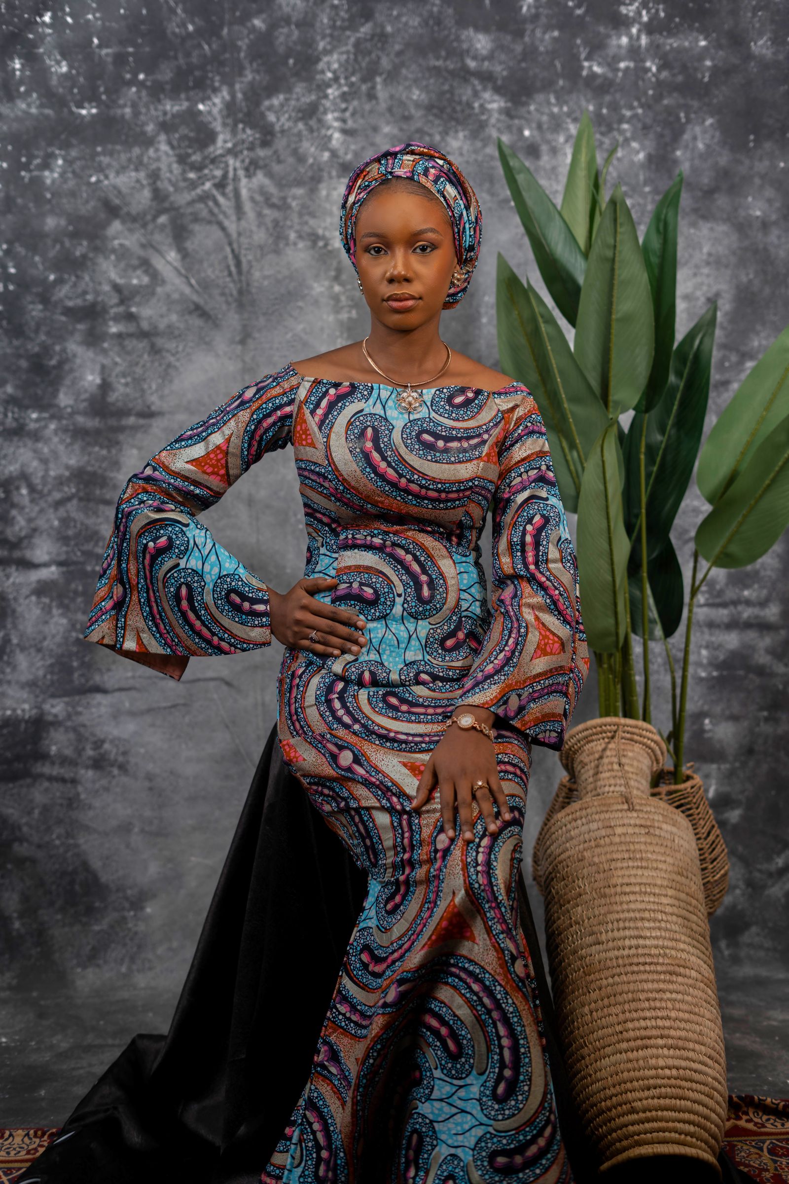 Woman in a patterned Kitenge dress with flared sleeves against a grey studio backdrop