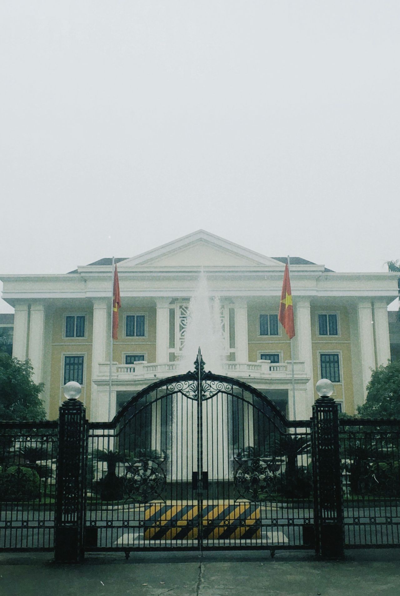 A grand historic building with flags and a central fountain, set behind intricate gates.