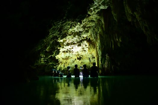 A group explores a dimly lit cave with illuminated waters, offering a mystical adventure.