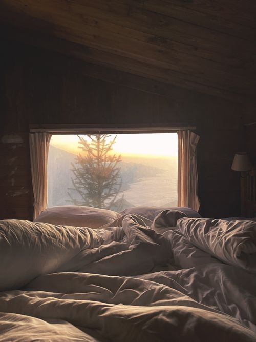 Free A serene bedroom with a view of sunrise through a large window in a rustic cabin. Stock Photo