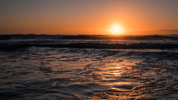Stunning sunset over a calm ocean with golden reflections on water. Peaceful beach scene.