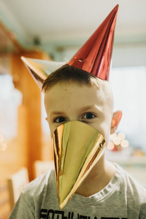 Free A cheerful child wears colorful party hats, embodying a fun festive atmosphere indoors. Stock Photo