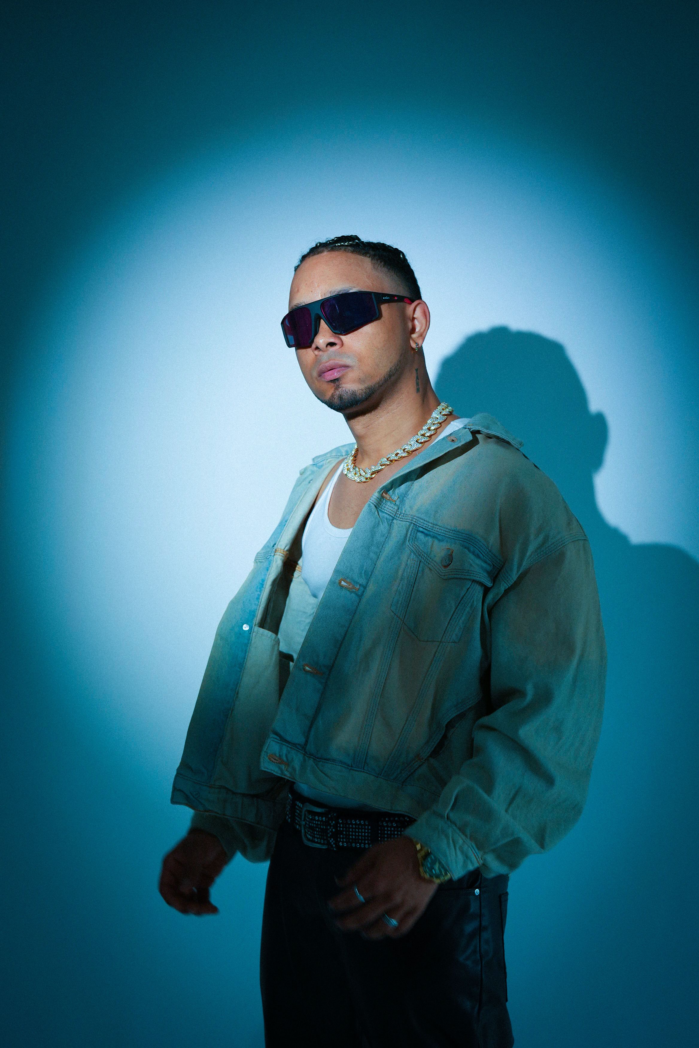A stylish young adult poses with sunglasses, highlighted by dramatic lighting.