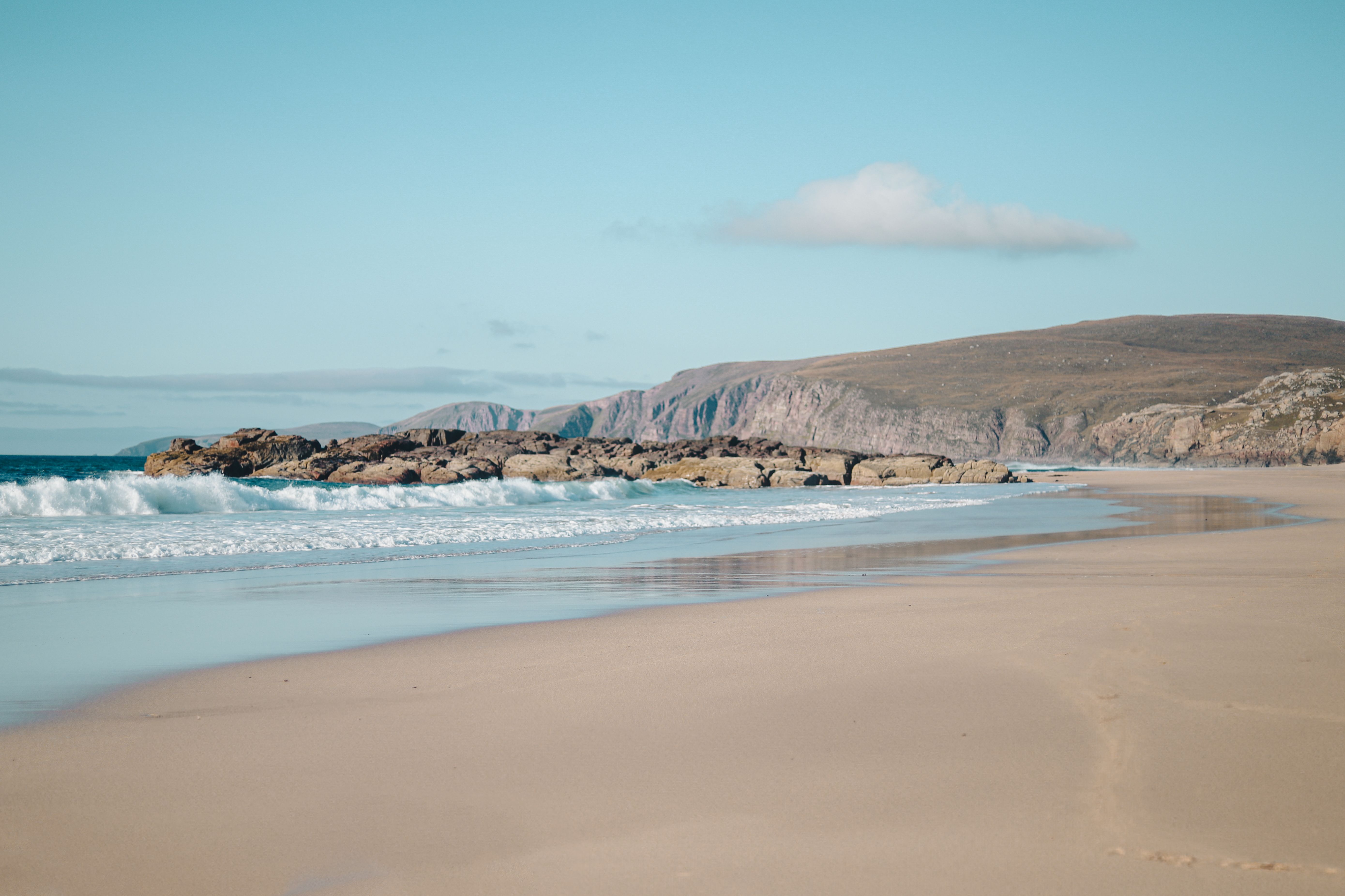 An empty white-sand beach with turquoise surf and headland cliffs