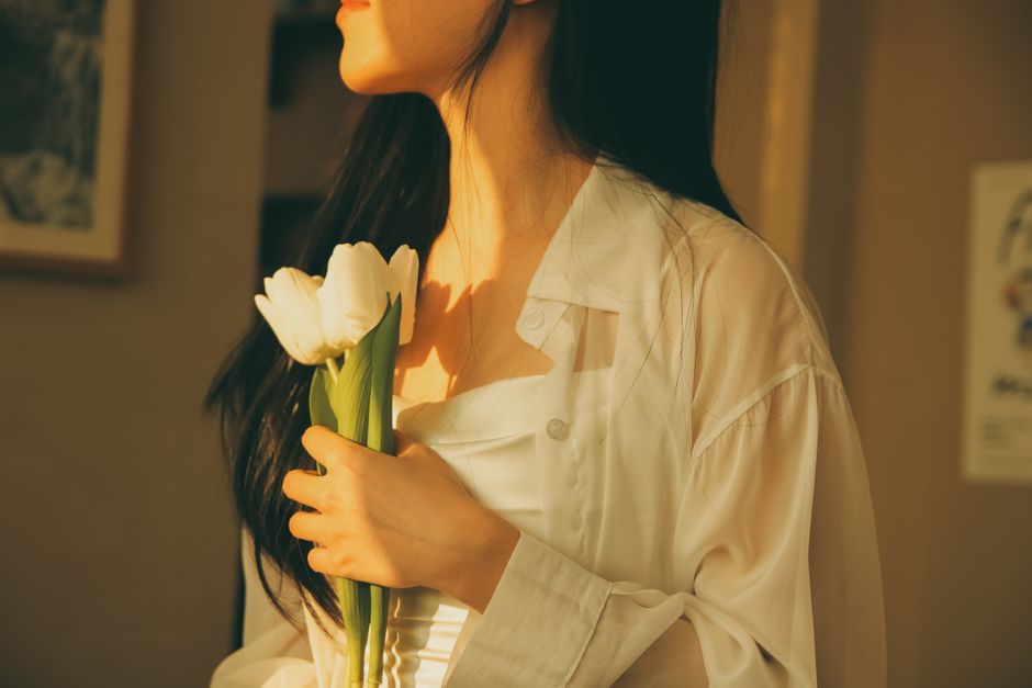 A woman in white holding tulips in soft, warm light, evoking serenity and elegance.