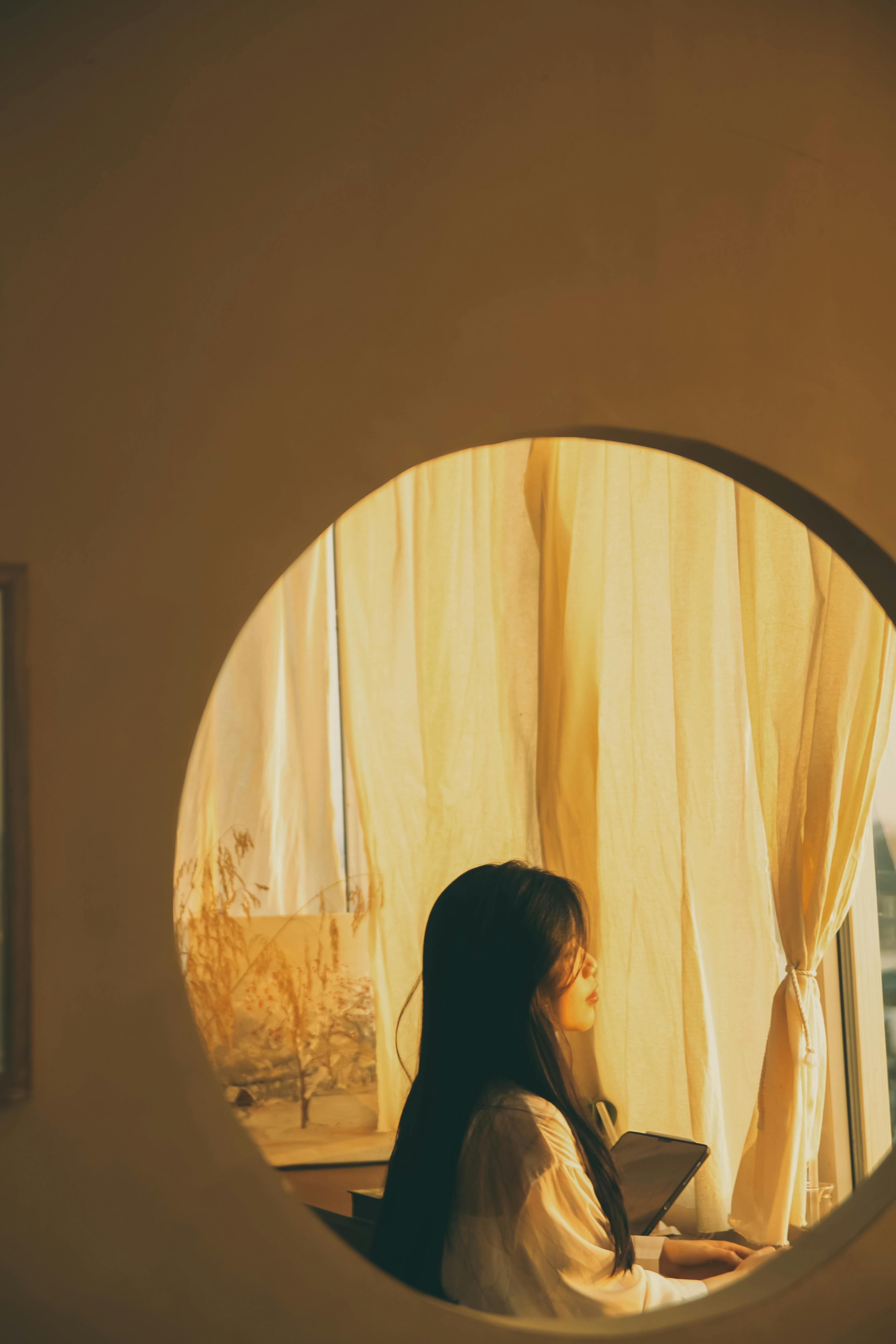A serene young woman looking out of a window, bathed in warm sunlight.