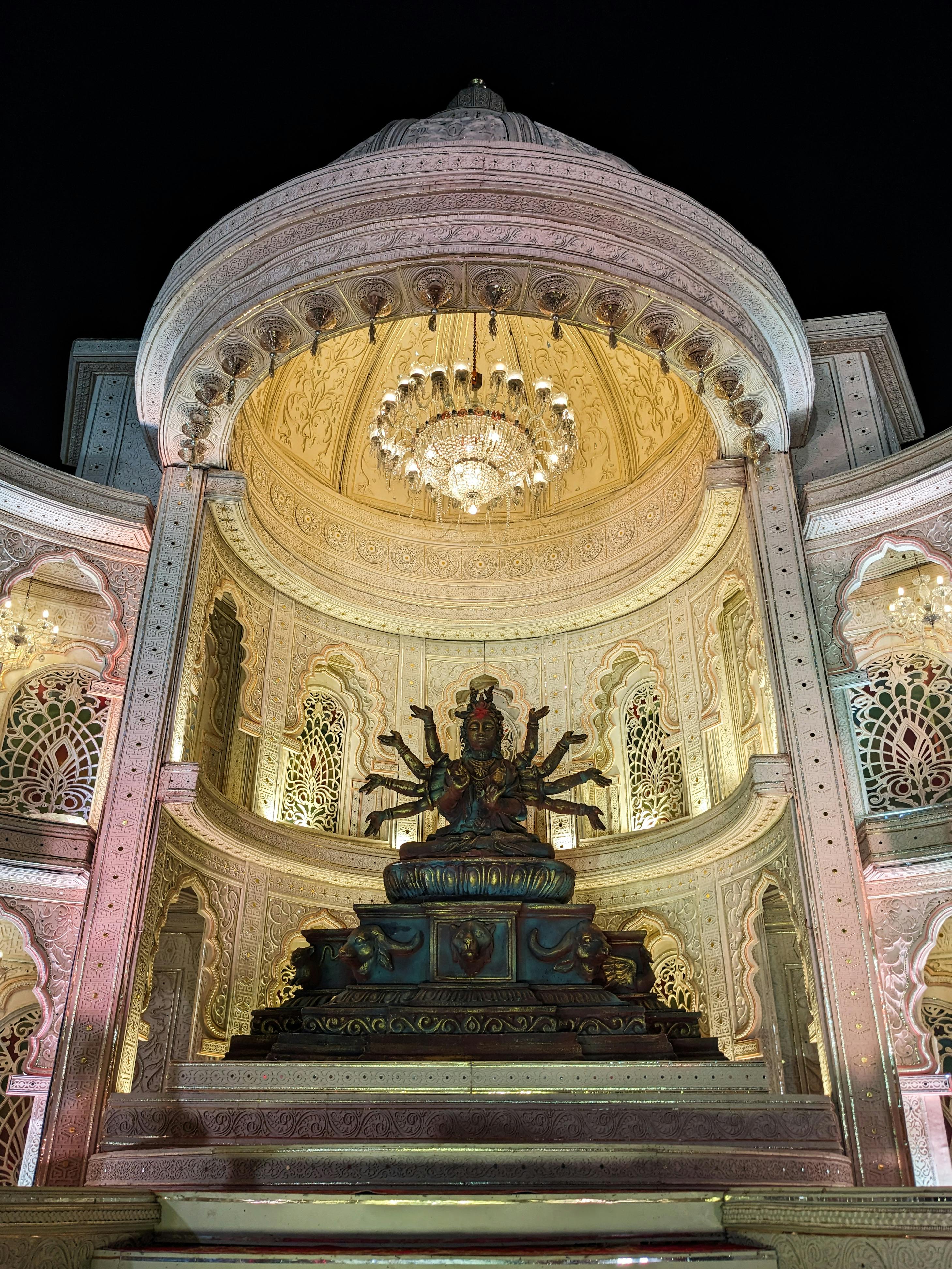 Kostnadsfria Nattvy av ett utsmyckat tempel som visar upp en gudomsskulptur, upplyst under en storslagen ljuskrona. Stock foto