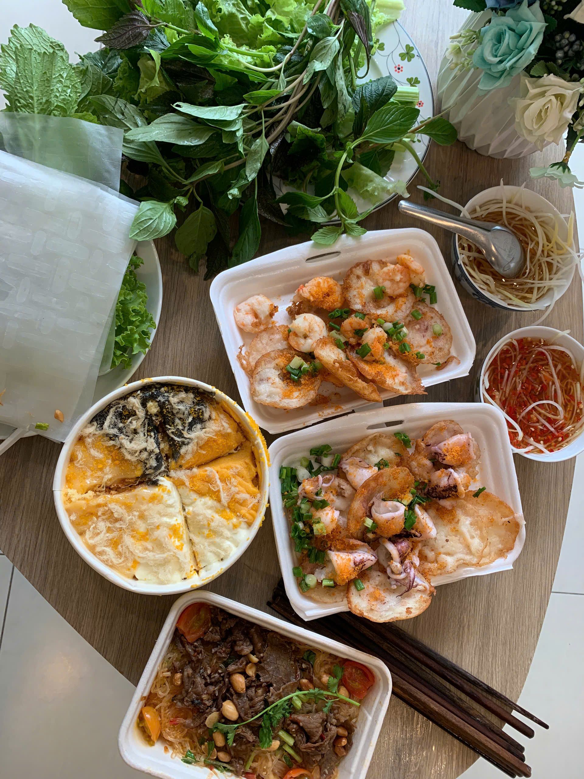 A colorful spread of Vietnamese dishes with fresh herbs and rice paper on a wooden table.