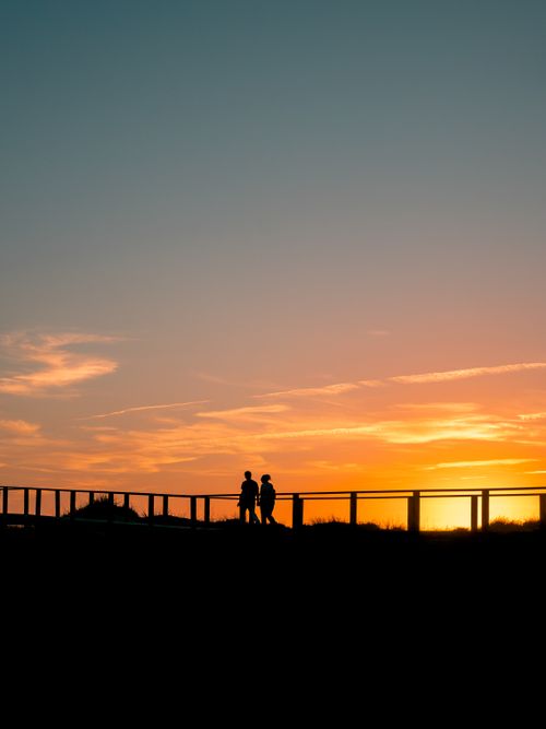 Free Silhouette of a couple walking at sunset on a boardwalk, capturing a peaceful and romantic moment. Stock Photo