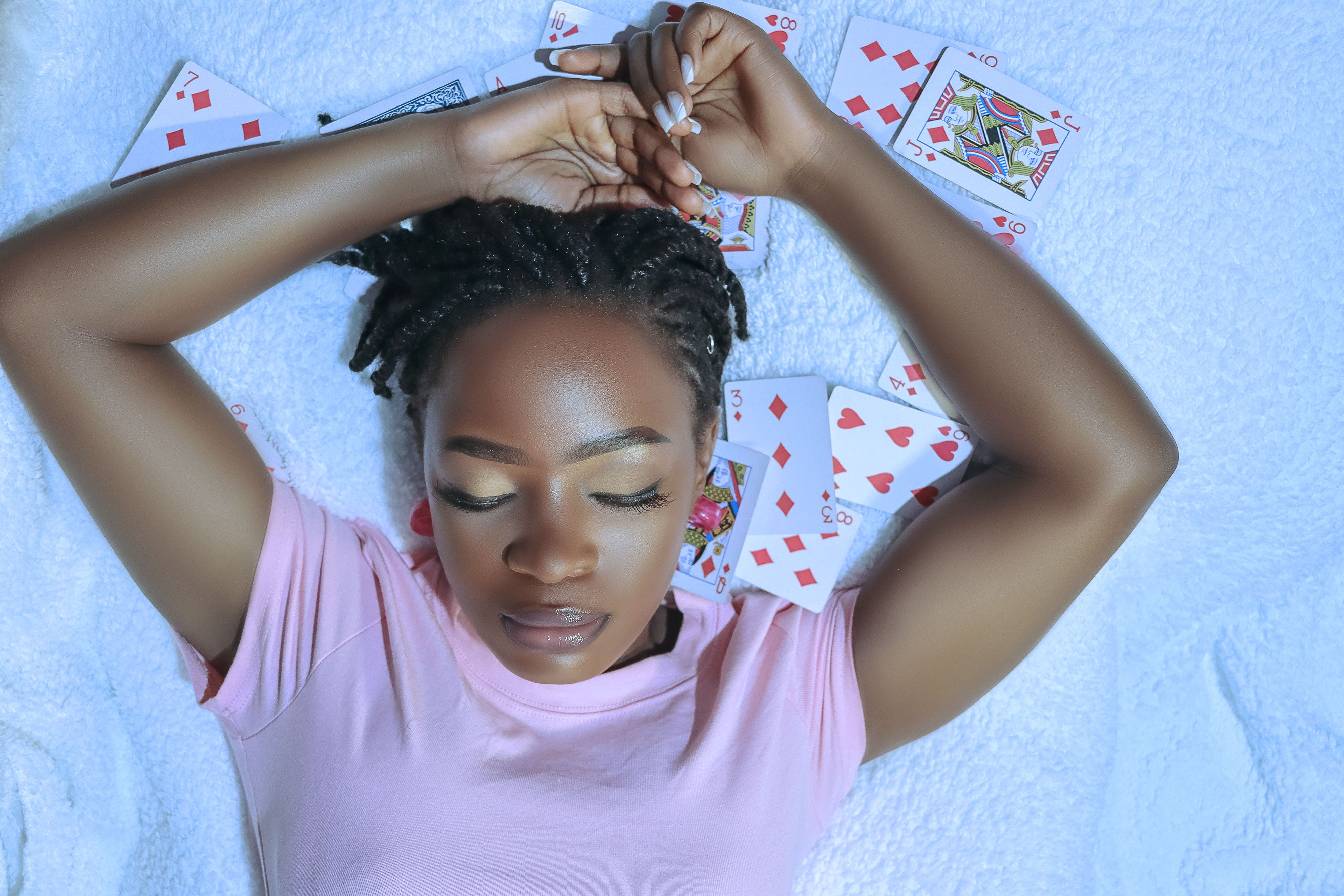 A woman in pink shirt lying on a soft surface surrounded by playing cards, looking serene.