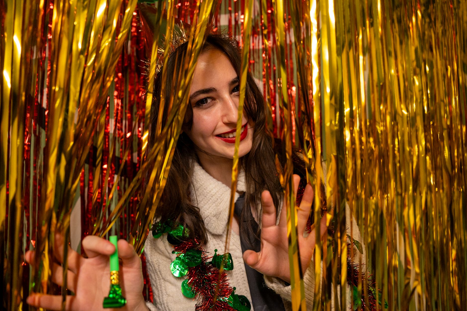 Young woman celebrates surrounded by vibrant gold and red tinsel for a festive occasion.