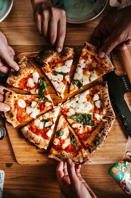 Hands reaching for freshly baked sourdough pizza slices in a lively gathering in London.