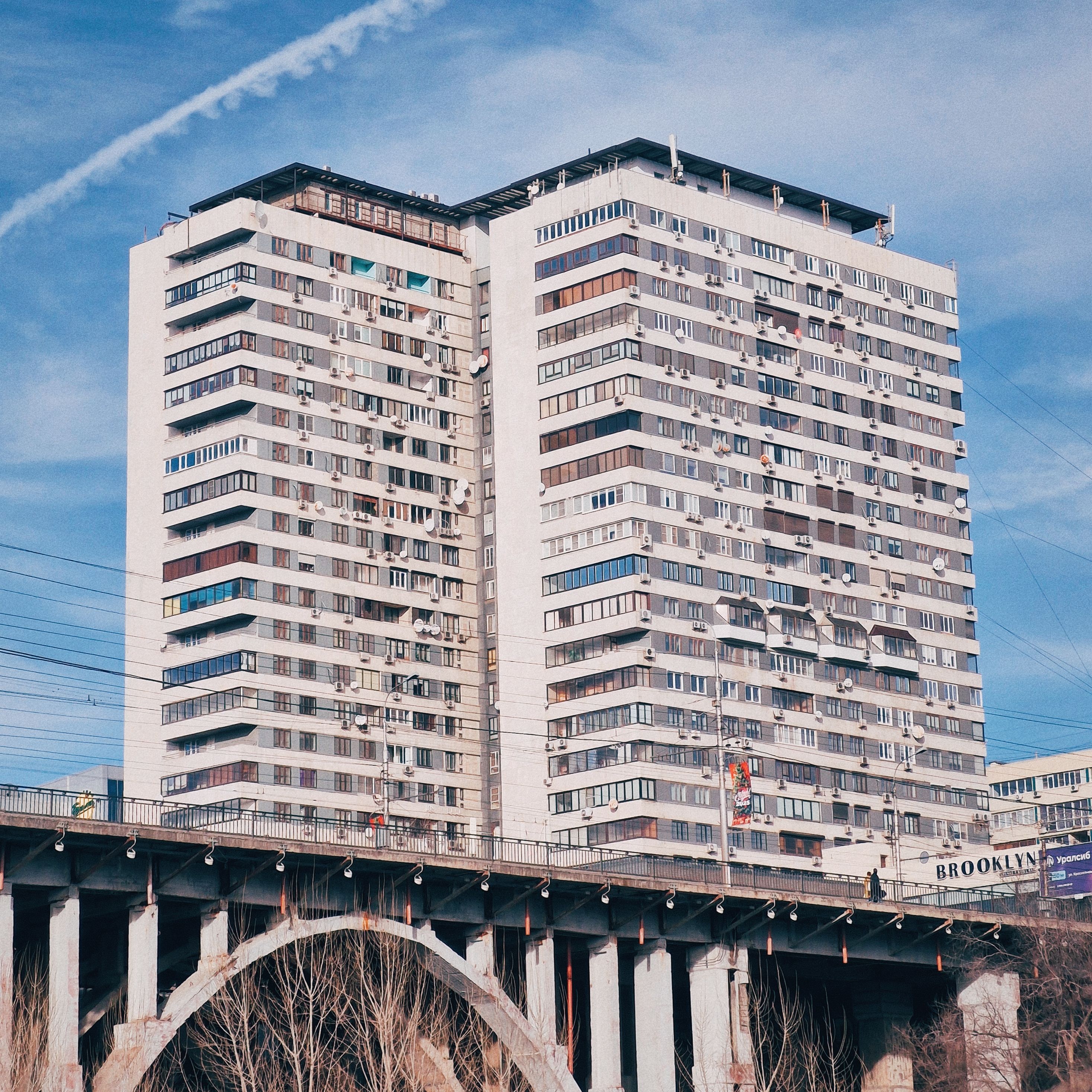 Cityscape with a tall apartment building and a bridge under clear skies.