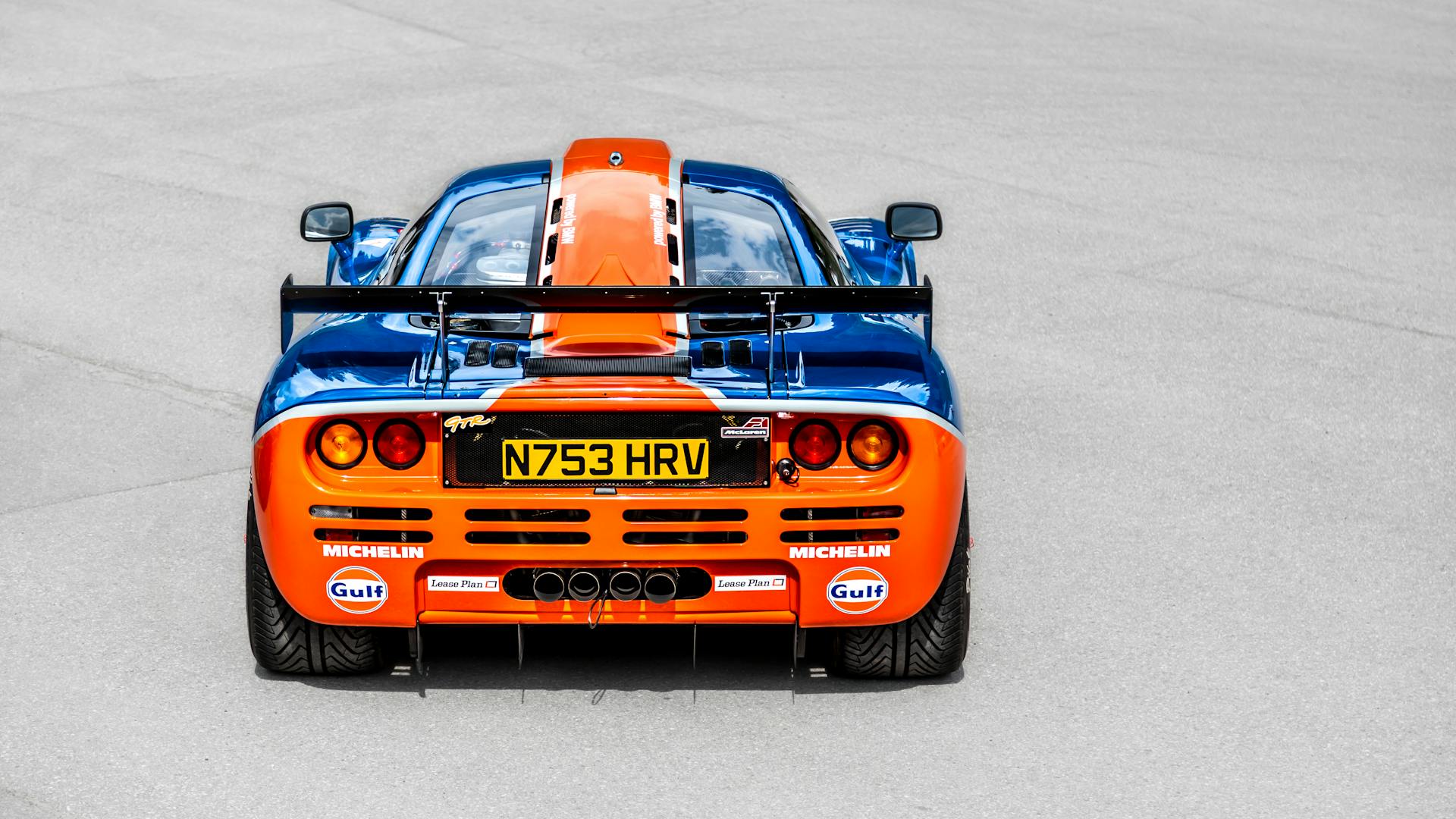 A striking rear view of a classic blue and orange McLaren sports car on display.