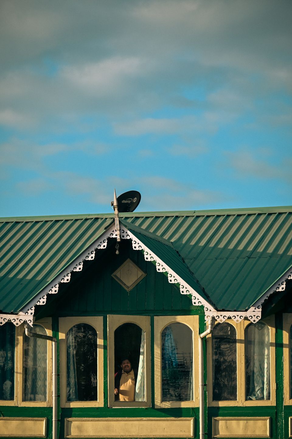 A green painted colonial house in Darjeeling with white fretwork eaves and arched verandah windows