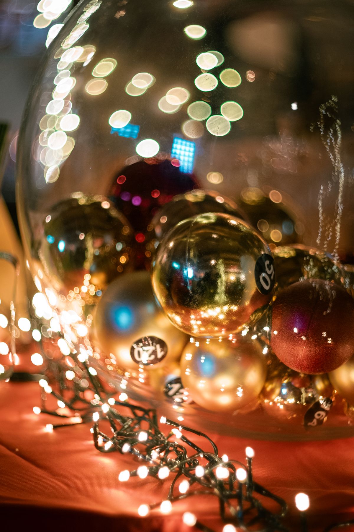 Gold and red Christmas ornaments in a large glass bowl wrapped in glowing fairy lights