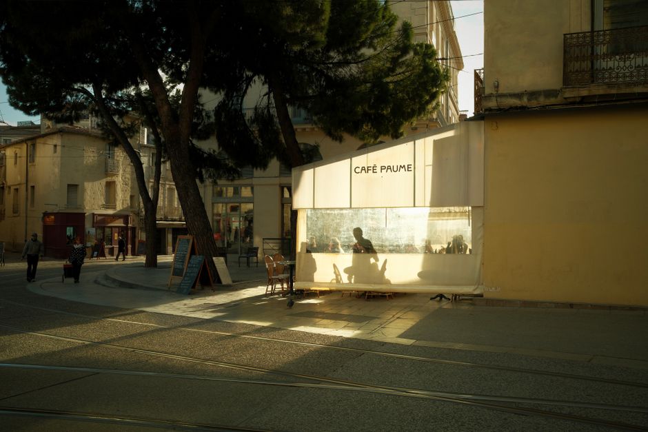 A serene street scene with shadows of patrons at Café Paume enjoying the warm afternoon sunlight.