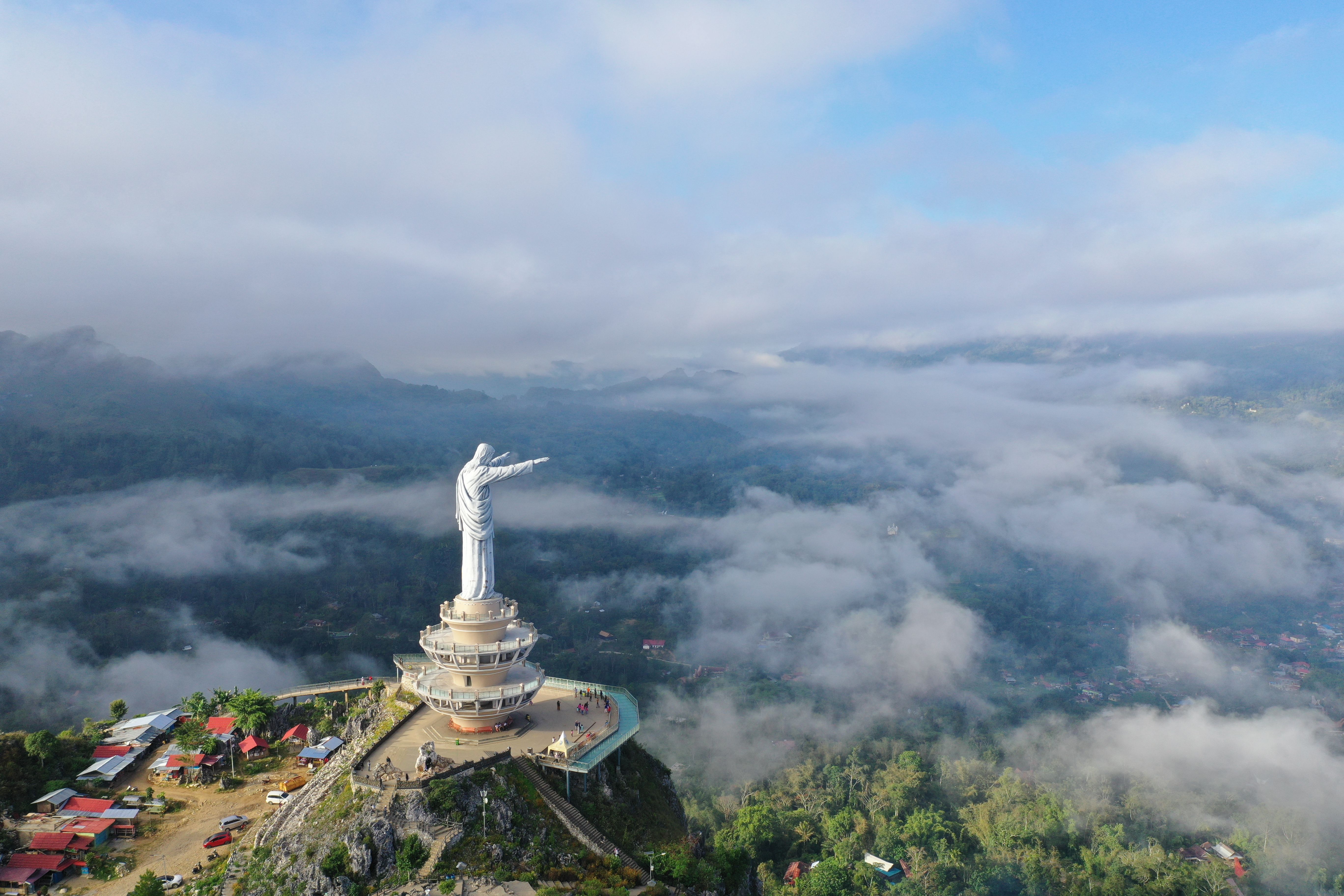 Breathtaking aerial view of the Jesus Buntu Burake statue surrounded by clouds in Sulawesi.