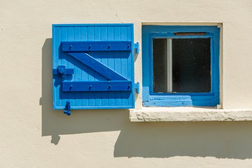 Free Bright blue shutter casting shadows on a cream-colored building facade, creating a vibrant contrast. Stock Photo