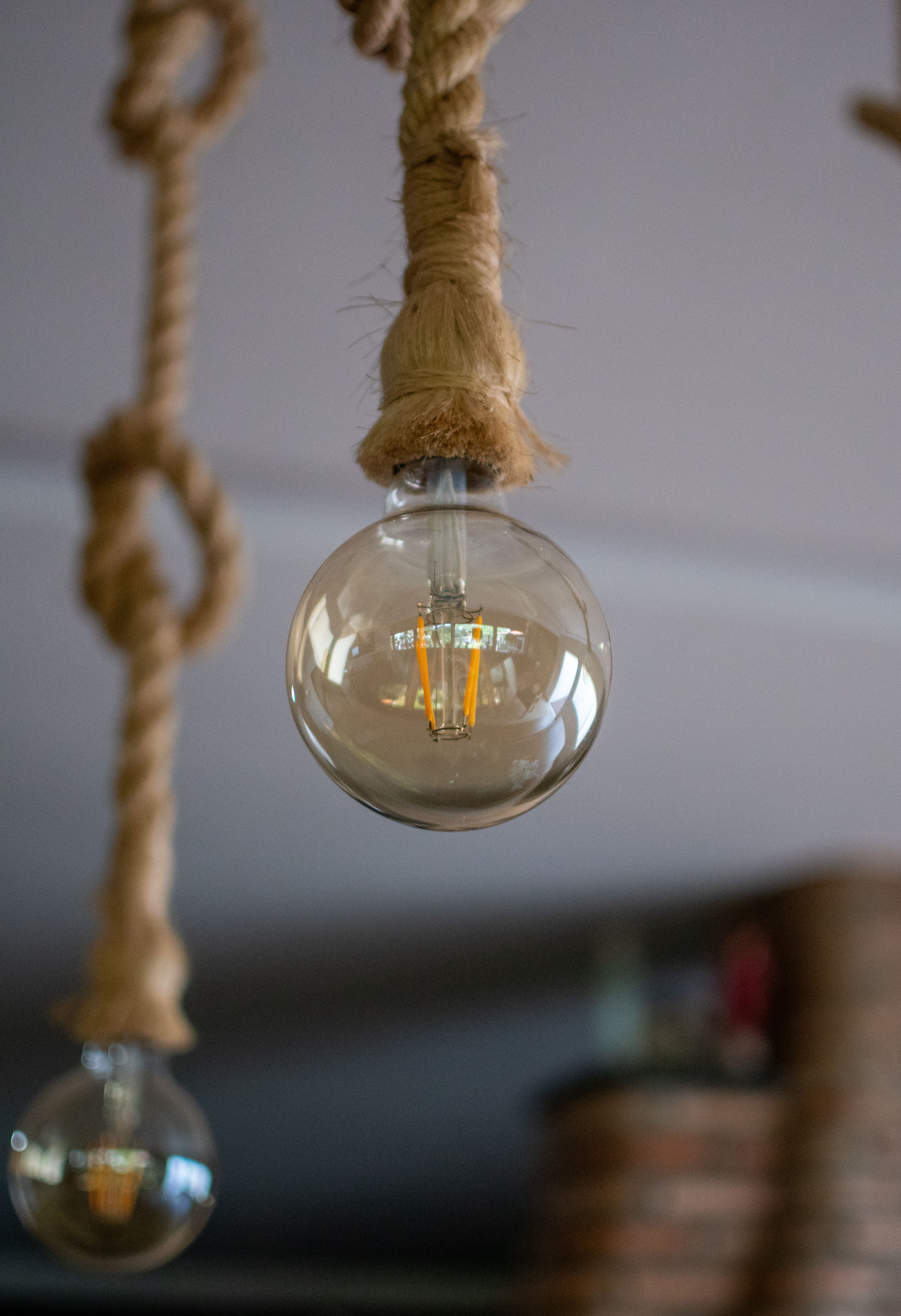 Close-up of a vintage Edison bulb hanging from a decorative rope indoors.