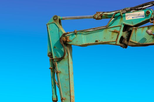 Detailed view of a turquoise excavator arm against a vivid blue sky.