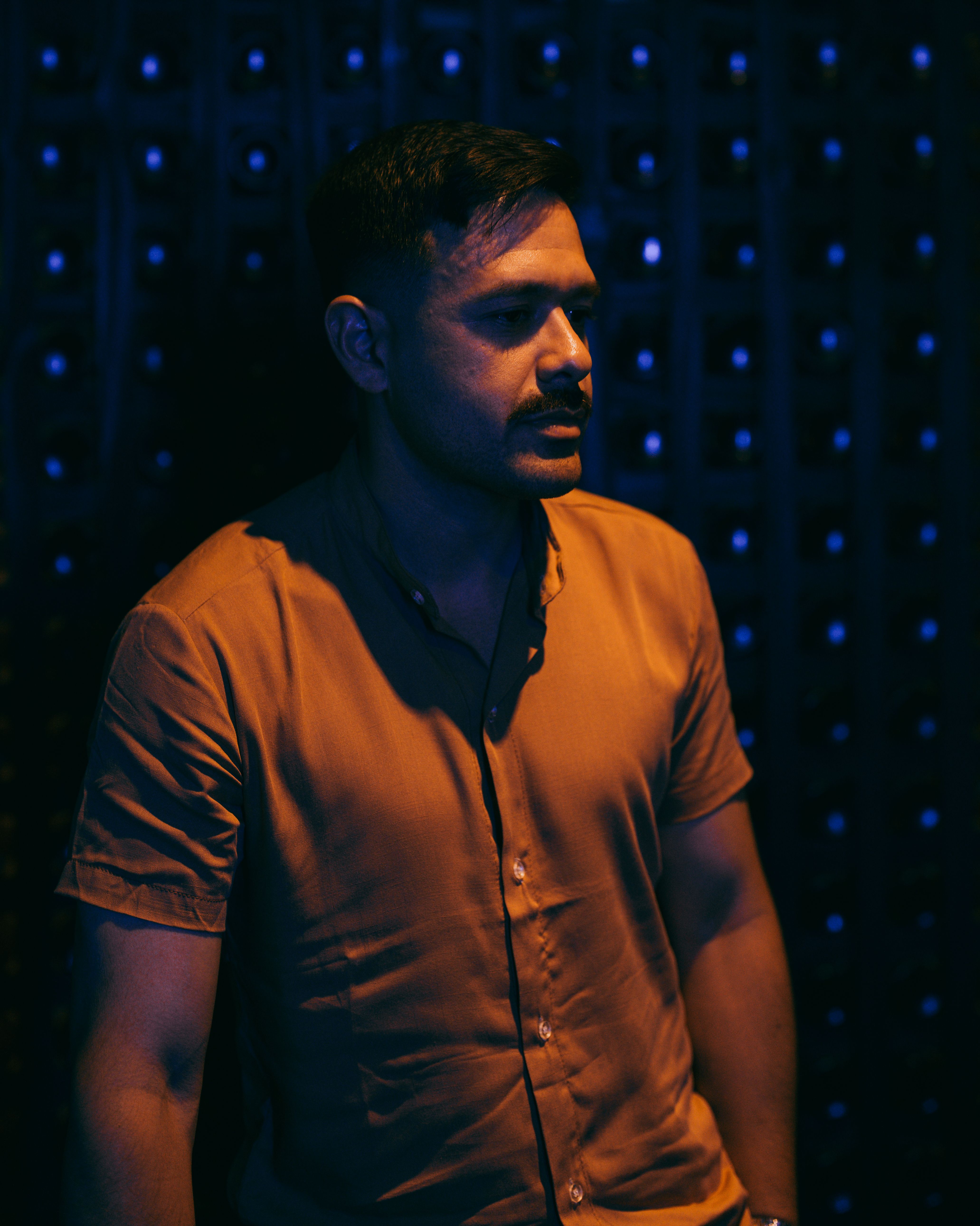 A man stands in low light with dramatic shadows, creating a moody atmosphere.