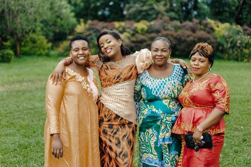 Free Four African women in colorful traditional dresses smiling and embracing each other outdoors. Stock Photo