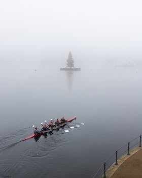 A rowing team glides through foggy Alster in Hamburg, Germany, with a distant Christmas tree in view.