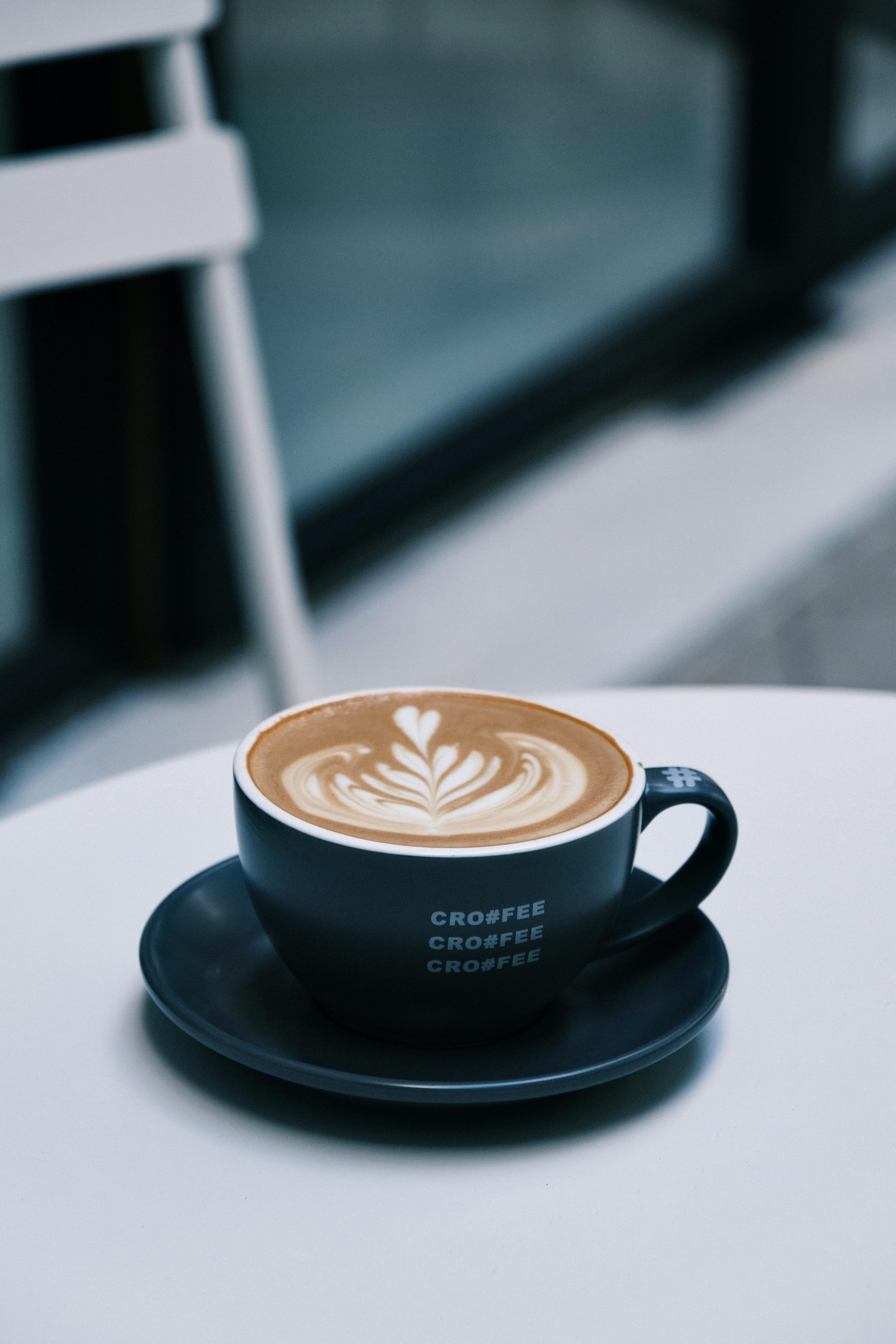 Close-up of a latte with artistic foam design on white table.